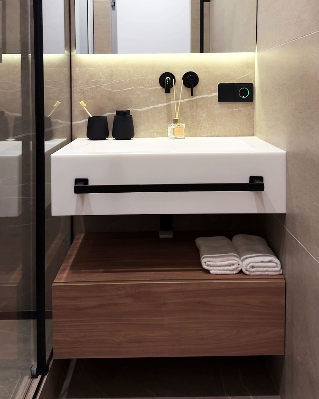 Білий умивальник зі штучного каменю, чорним змішувачем вбудованим в стіну, тумбою зі шпонованого МДФ