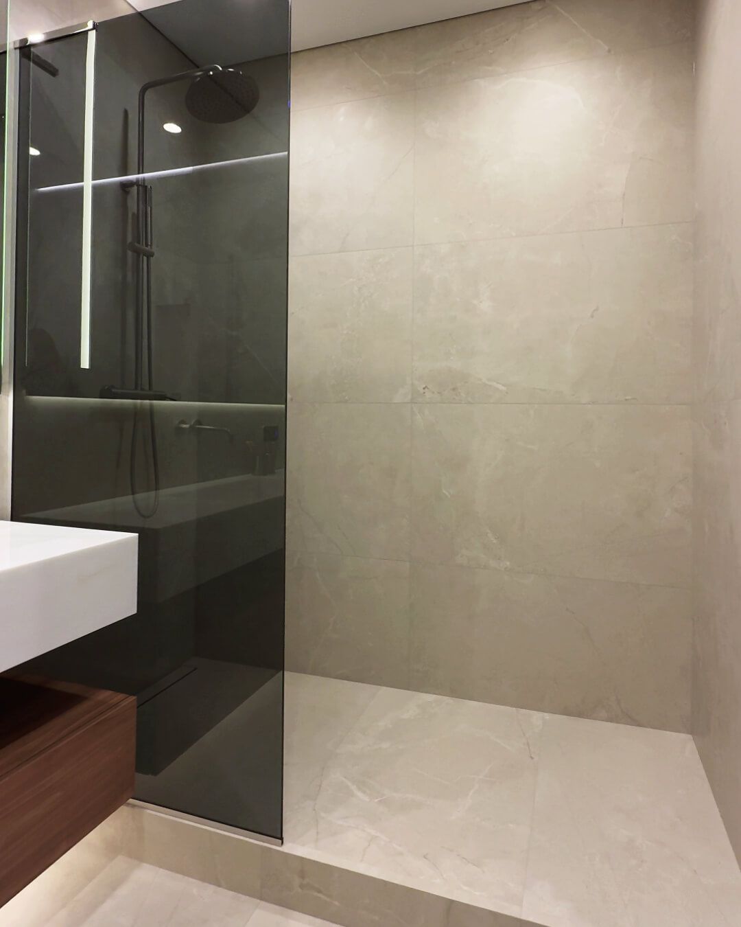 Широка душова з плиткою великого формату, перегородкою з затемненого скла, змішувач золотистого кольору