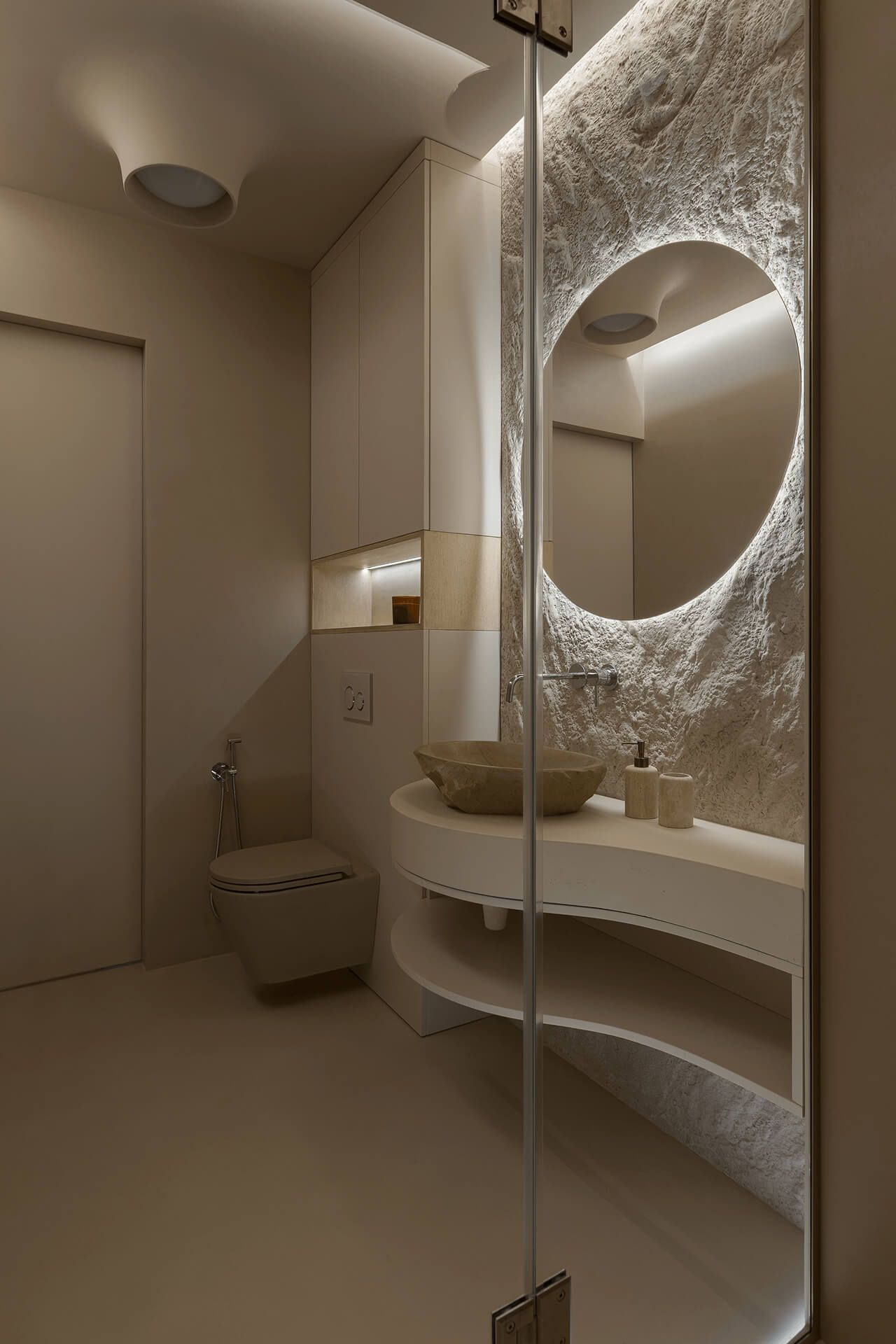 Бежева ванна кімната з кам’яним умивальником на хвилястій підвісній тумбі; декоративна штукатурка під скельну породу