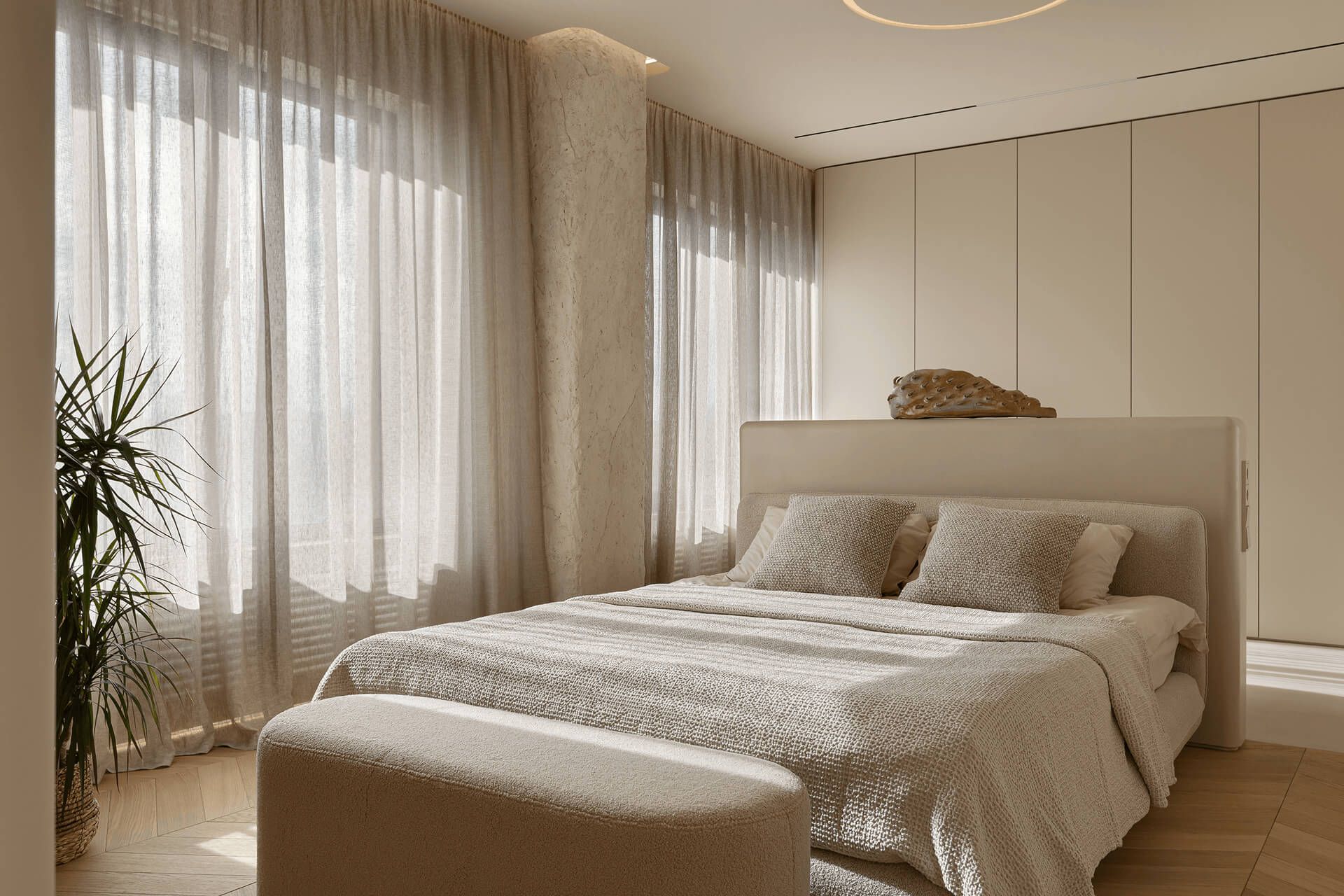 Інтер’єр спальні: ліжко з приліжковим пуфом, ванна за узолів'ям, напівпрозорі штори на великих вікнах