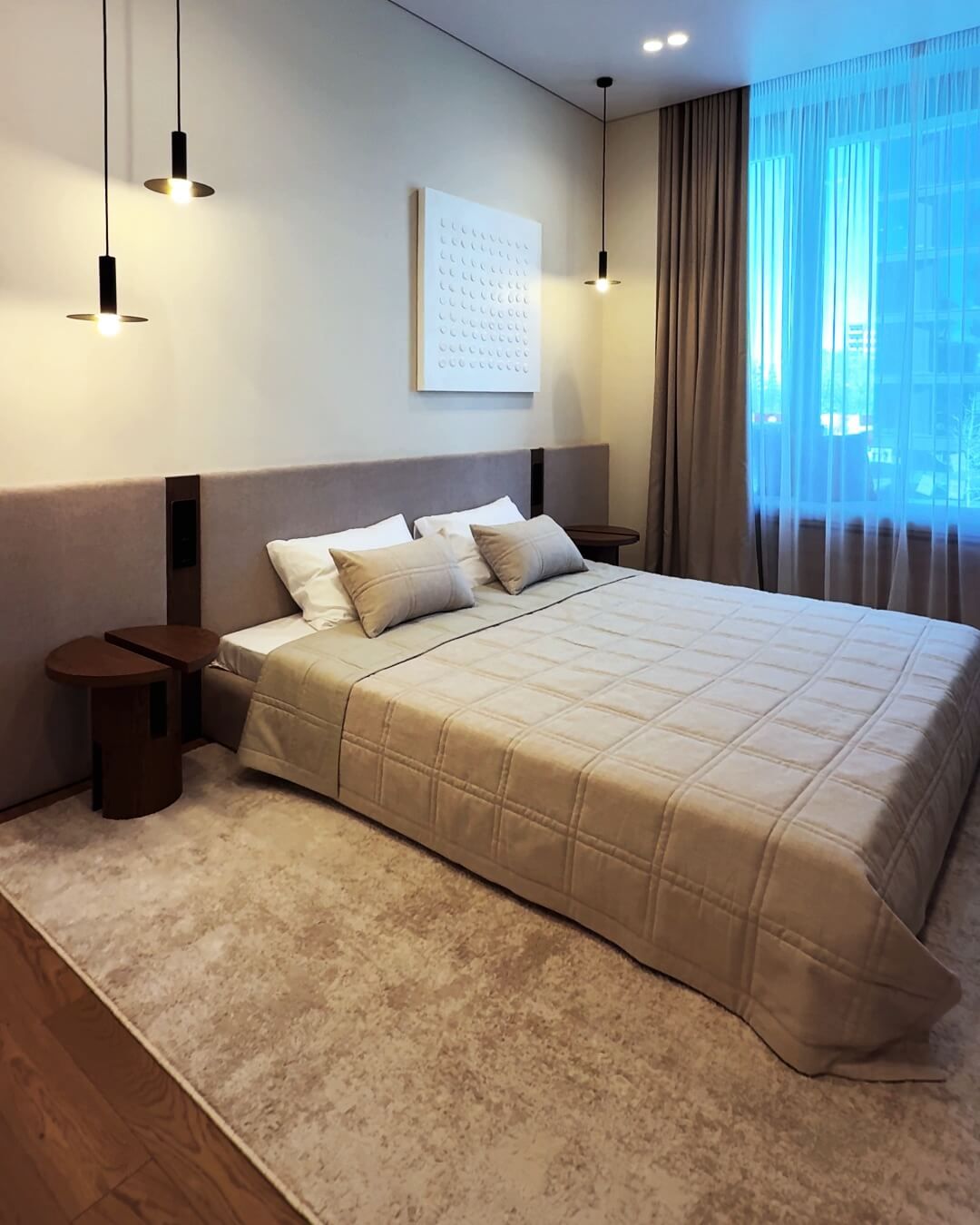 Спальня кімната зі стінами кремового кольору, м'якими стіновими панелями, чорними підвісними світильниками