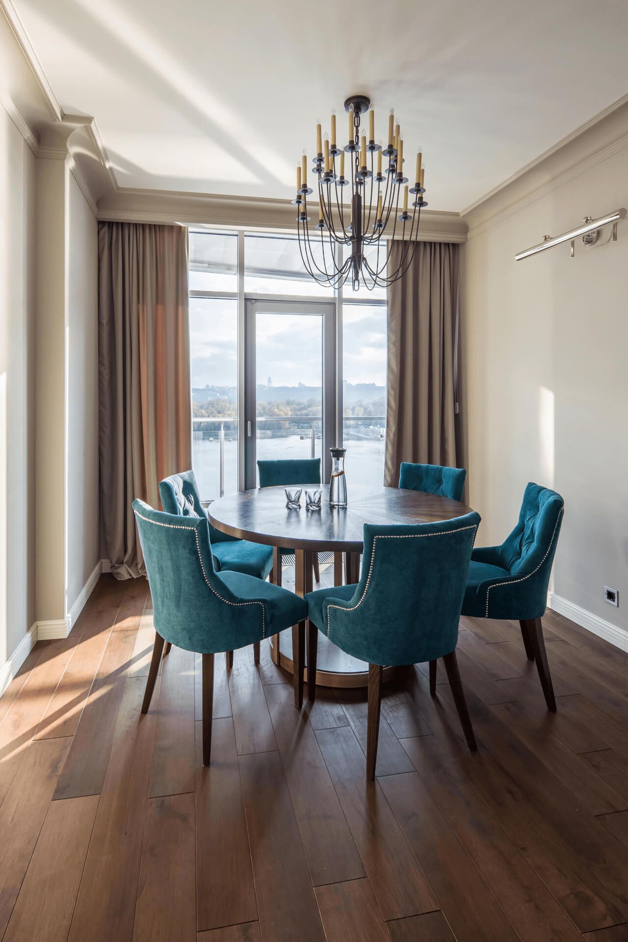 Інтер'єр їдальні з круглим дерев’яним столом, м’якими стільцями та дизайнерською люстрою