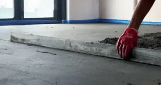 Процес влаштування цементно-піщаної стяжки, майстер вирівнює правилом поверхню