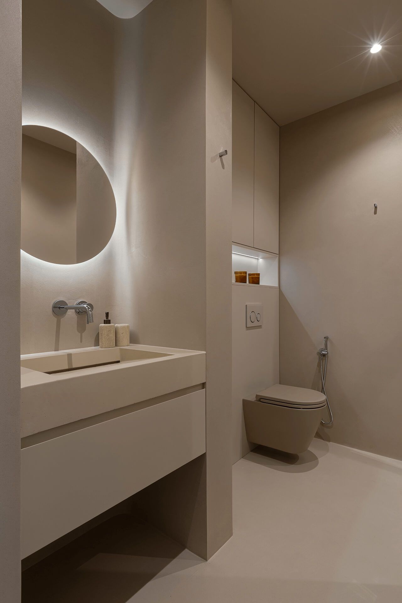 Санвузол бежевого відтінку: підвісна тумба із вбудованим умивальником; над інсталяцією декоративна ніша з підсвіткою та шафа