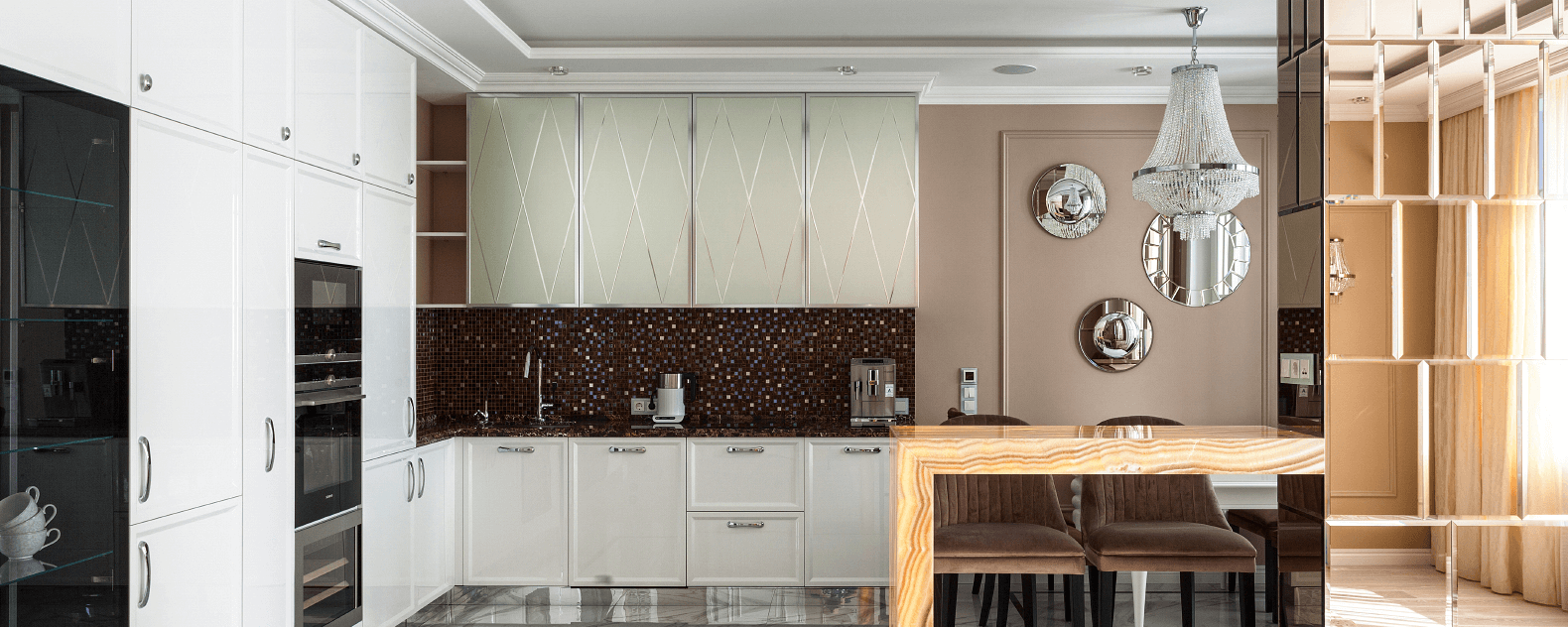 Інтер’єр кухні-вітальні з фасадами кремового кольору, мозаїкою на робочій зоні і люстрою в красичному стилі