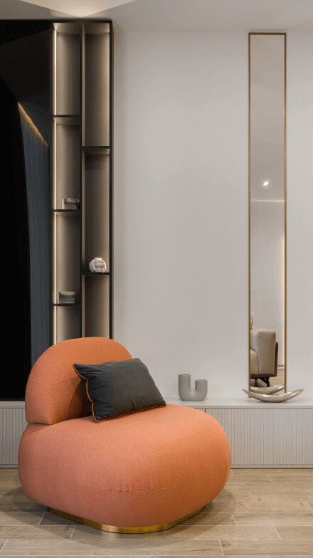 М'яке крісло помаранчевого кольору, високе декоративне дзеркало, полички з підсвіткою