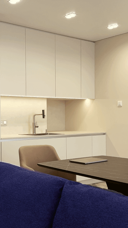 Кухня-вітальня вільного планування, стіни та кухонні фасади світлі, м'які крісла-стільці, темного кольору стіл