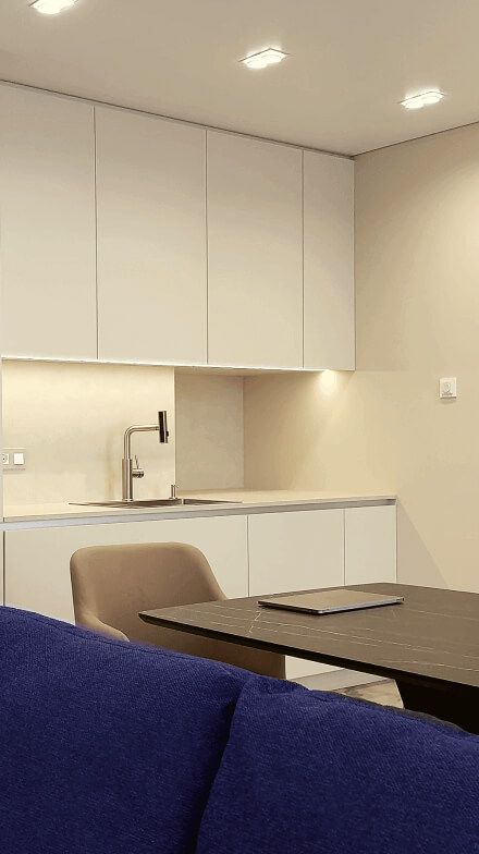 Кухня-вітальня вільного планування, стіни та кухонні фасади світлі, м'які крісла-стільці, темного кольору стіл