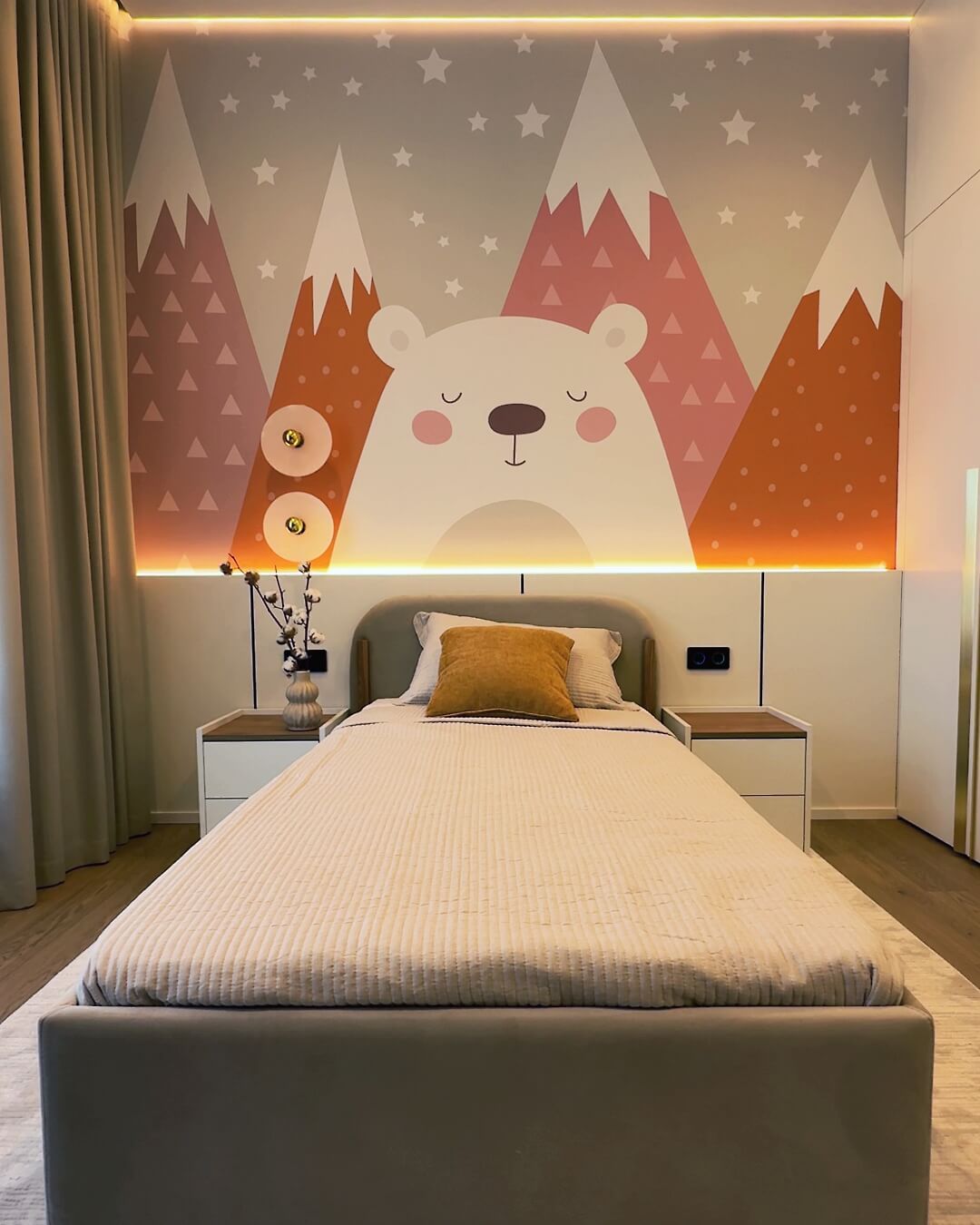 Інтер'єр дитячої кімнати з яскравою стіною із зображенням ведмедика та гір за узголів'ям ліжка