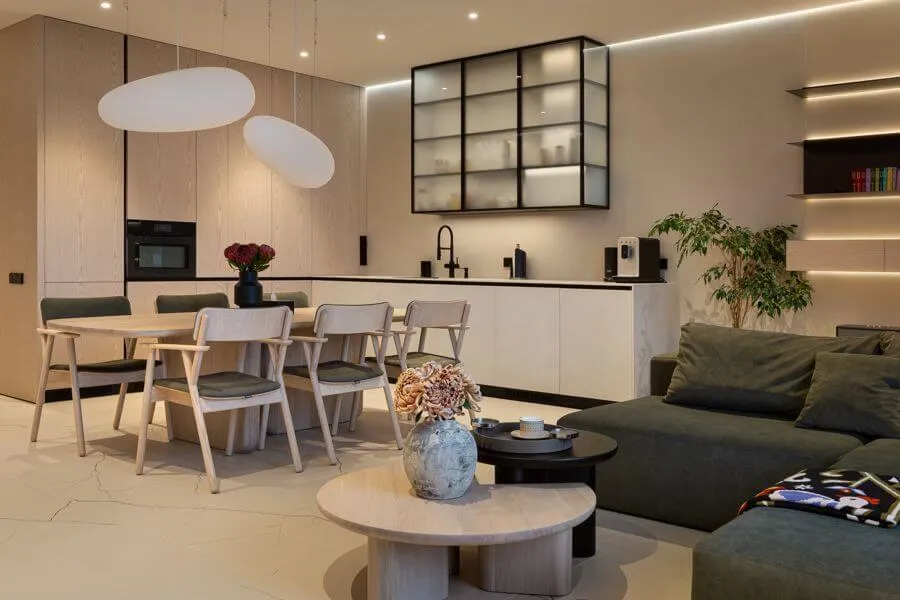 Кухня-вітальня з кухонними фасадами зі шпонованого МДФ та інтегрованою технікою, дерев’яними обіднім столом і стільцями та модульним диваном