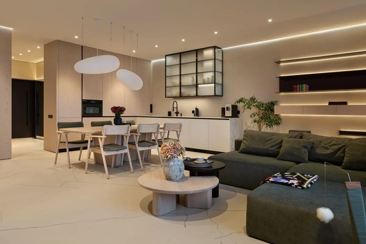 Кухня-вітальня з кухонними фасадами зі шпонованого МДФ та інтегрованою технікою, дерев’яними обіднім столом і стільцями та модульним диваном