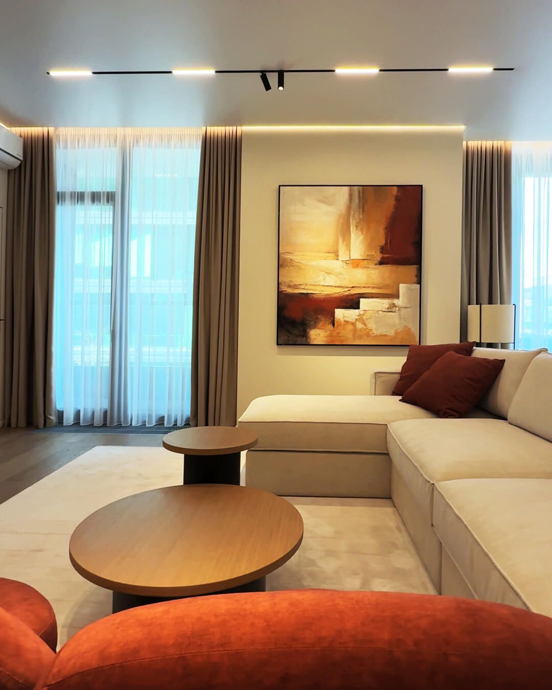 Інтер'єр вітальні в Києві після ремонту з бежевим диваном, картиною та трековим освітленням.