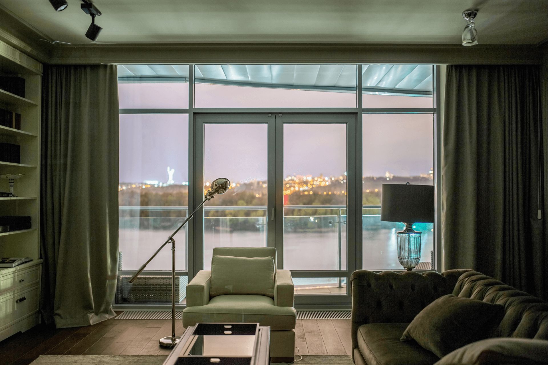 Вітальня з панорамними вікнами на Дніпро, м’яким диваном і кріслом, торшери