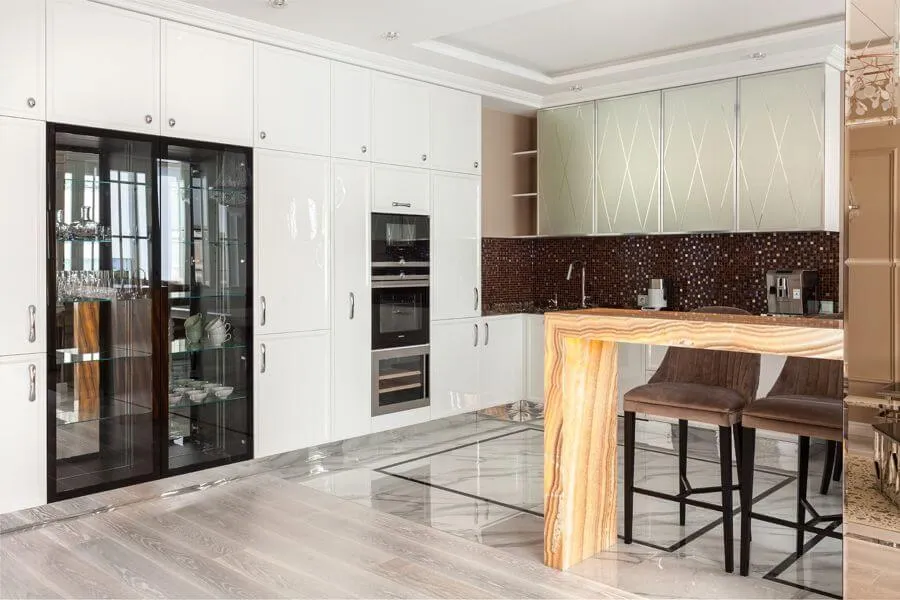 Кухня з білими фасадами і скляною вітриною для посуду, темним фартухом з мозаїки і барним столом