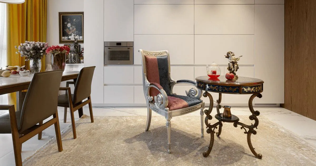 Крісло та столик в класичному стилі з різбленими ніжками, на столику декоративні фігури та скляний чайник; білі кухонні фасади