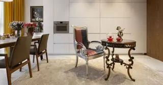 Крісло та столик в класичному стилі з різбленими ніжками, на столику декоративні фігури та скляний чайник; білі кухонні фасади