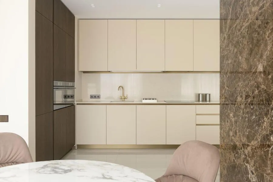 Кухня з темно-горіховими і кремовими фасадами, золотим змішувачем і акцентною стіною з керамограніту під коричневий мармур