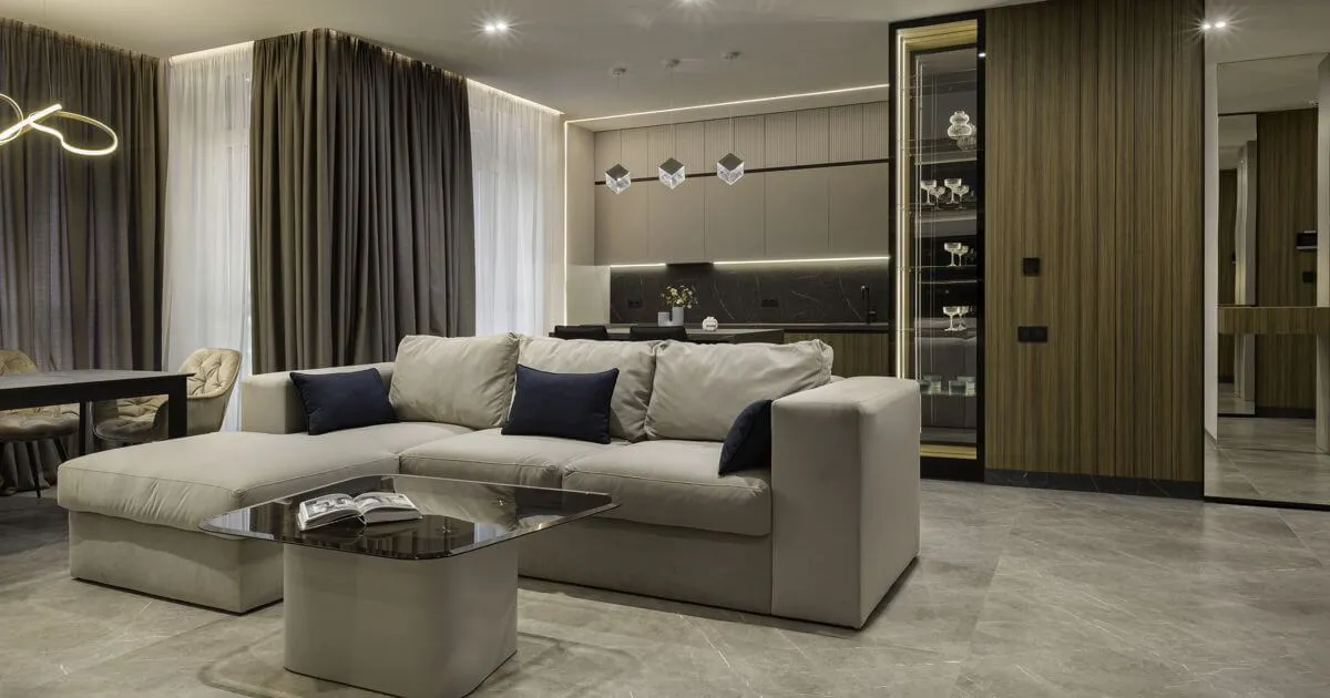 Інтер'єр кухні-вітальні в темних тонах з фасадом зі шпону, світильниками кубічної форми над островом, диваном і обідньої зоною біля вікна