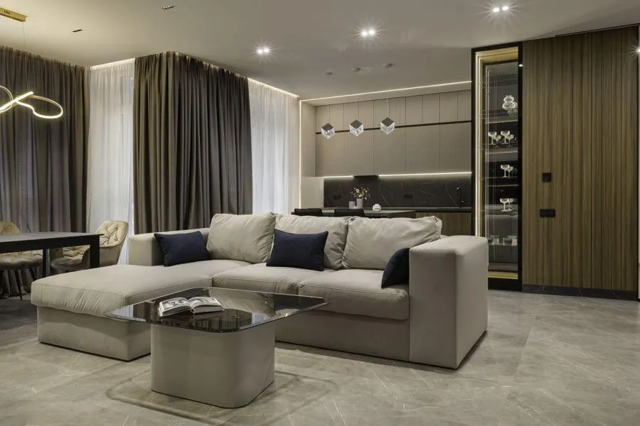 Інтер'єр кухні-вітальні в темних тонах з фасадом зі шпону, світильниками кубічної форми над островом, диваном і обідньої зоною біля вікна