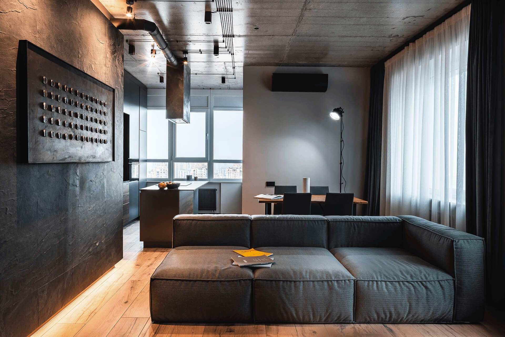 Кухня-вітальня з бетонною стелею, кам’яним шпоном на стінах та сучасним модульним диваном