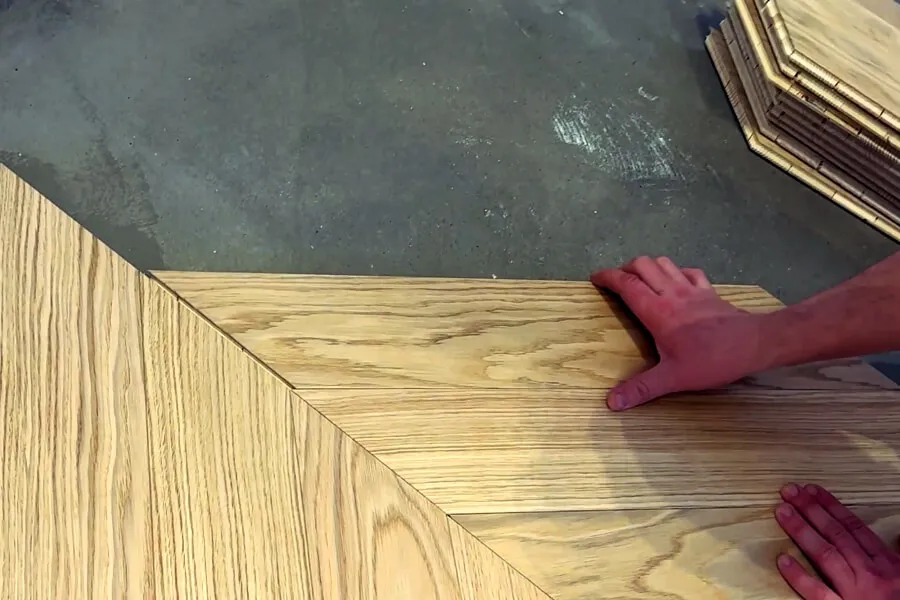 Процес укладання ялинкою паркетної дошки світлого дерева на підлогу