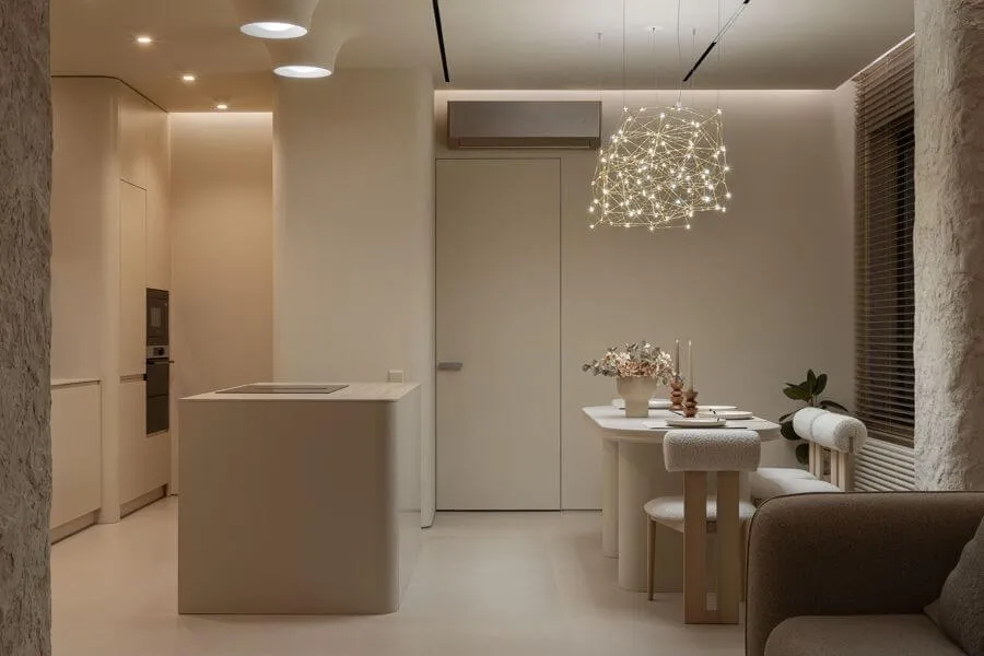 Декоративний світильник над обіднім столом як головний акцент, м’яке стельове підсвічування рівномірно освітлює кухню