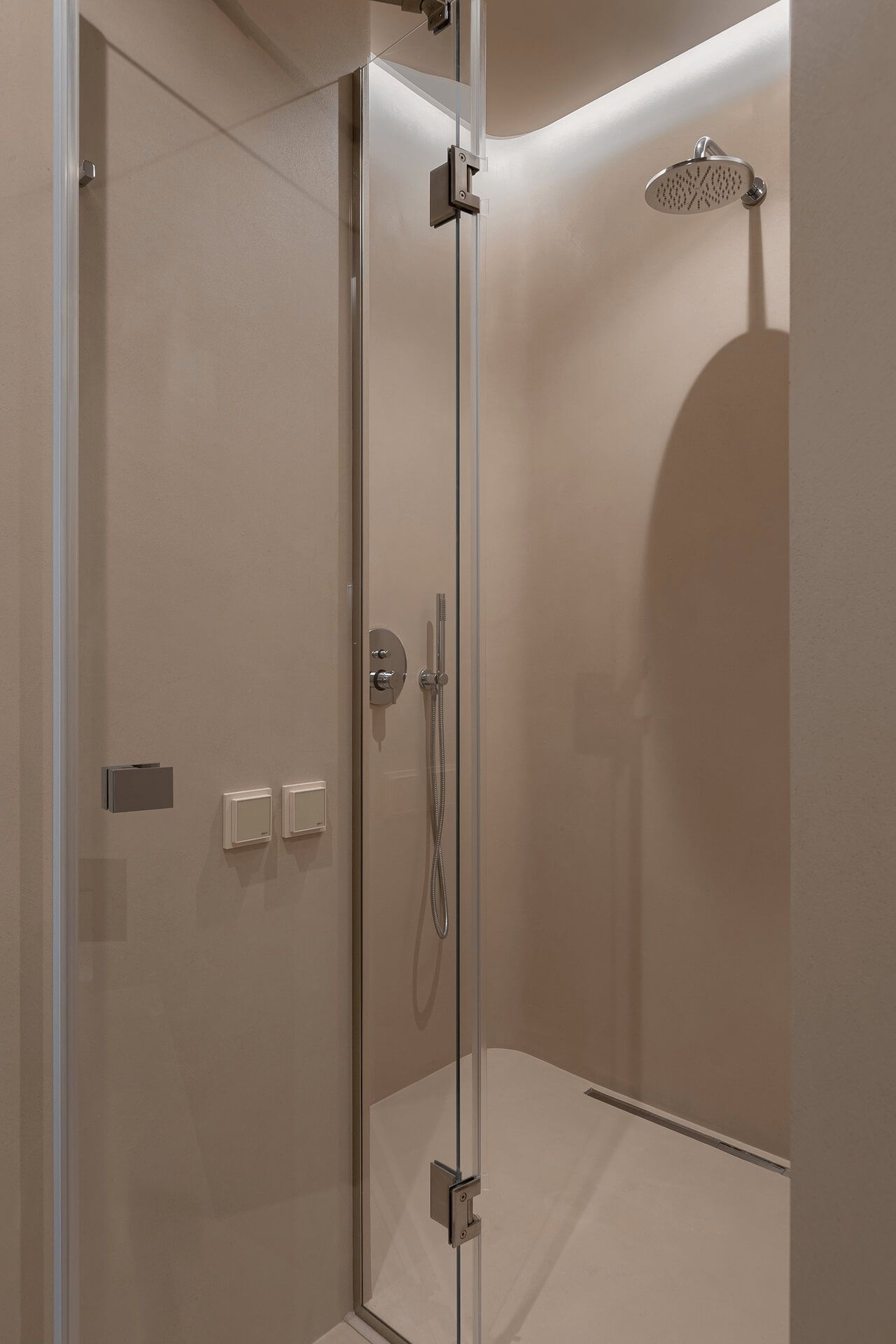 Душова кабіна з мікроцементними стінами теплого бежевого кольору, скляними дверима та хромованою сантехнікою