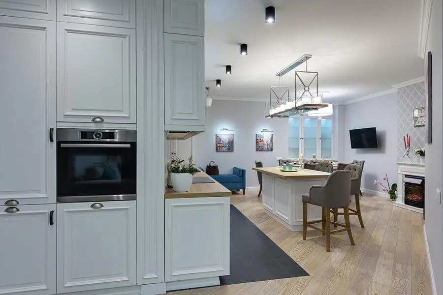 Світла кухня в стилі неокласика з кухонним островом, фрезерованими фасадами з металевими ручками-черепашками і декоративною люстрою